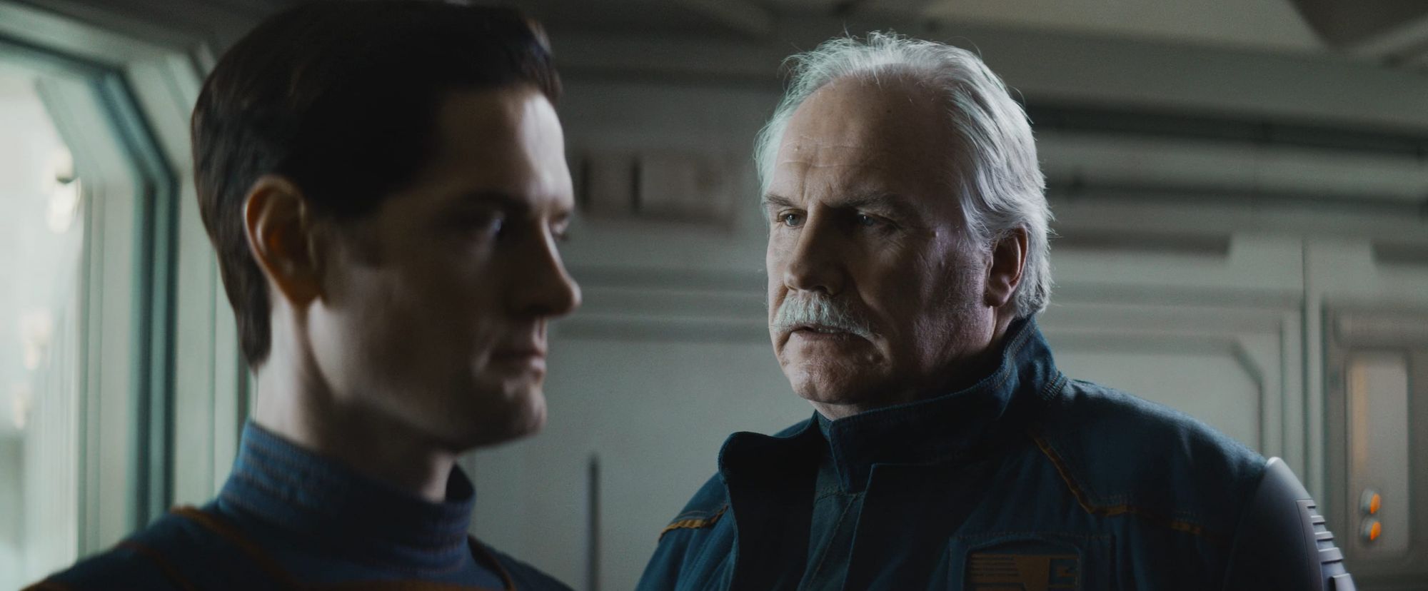 An older man talks to a younger man. They're both wearing uniforms, and it's clear the older man is lecturing the younger man.