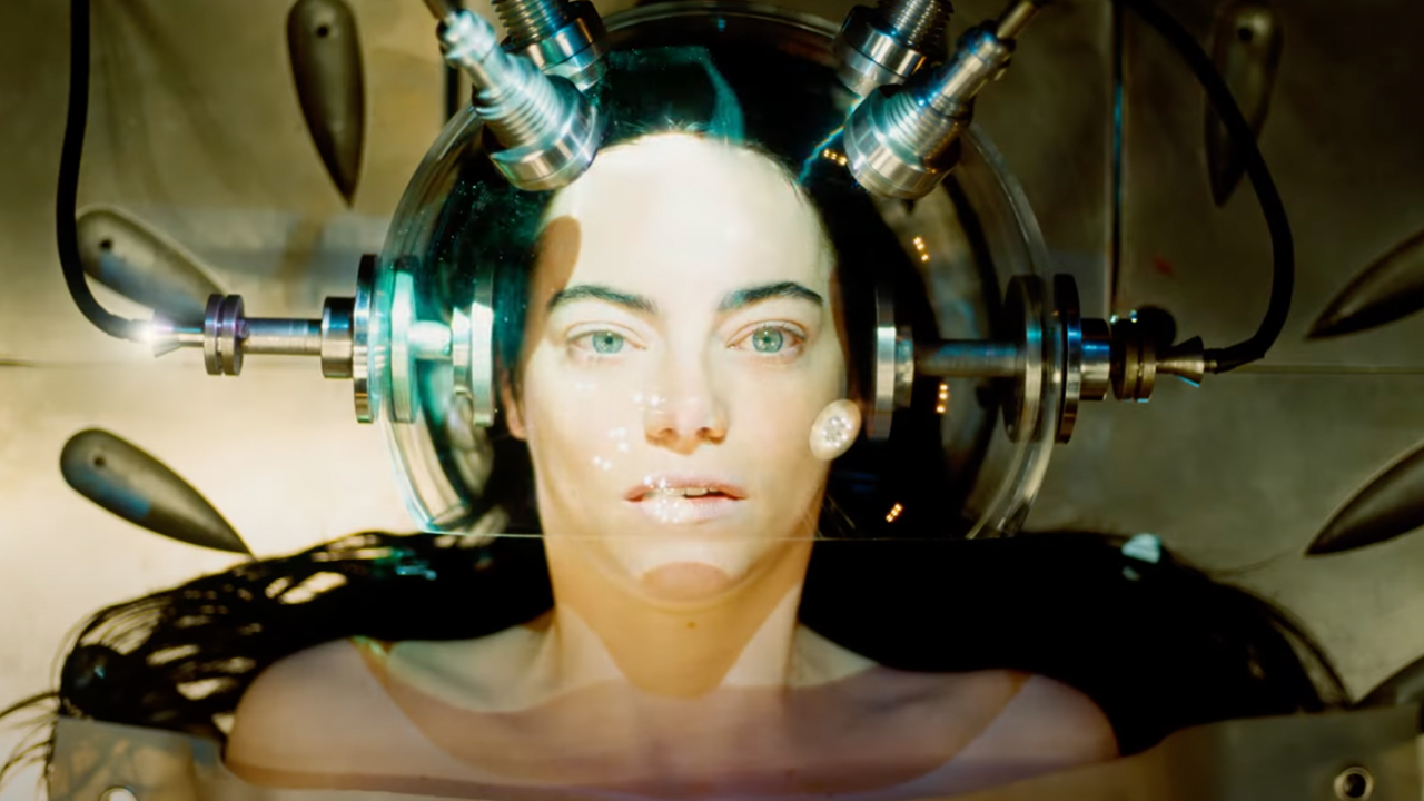 Bella lays on an operating table, her head surrounded by electric probes and a glass helmet.