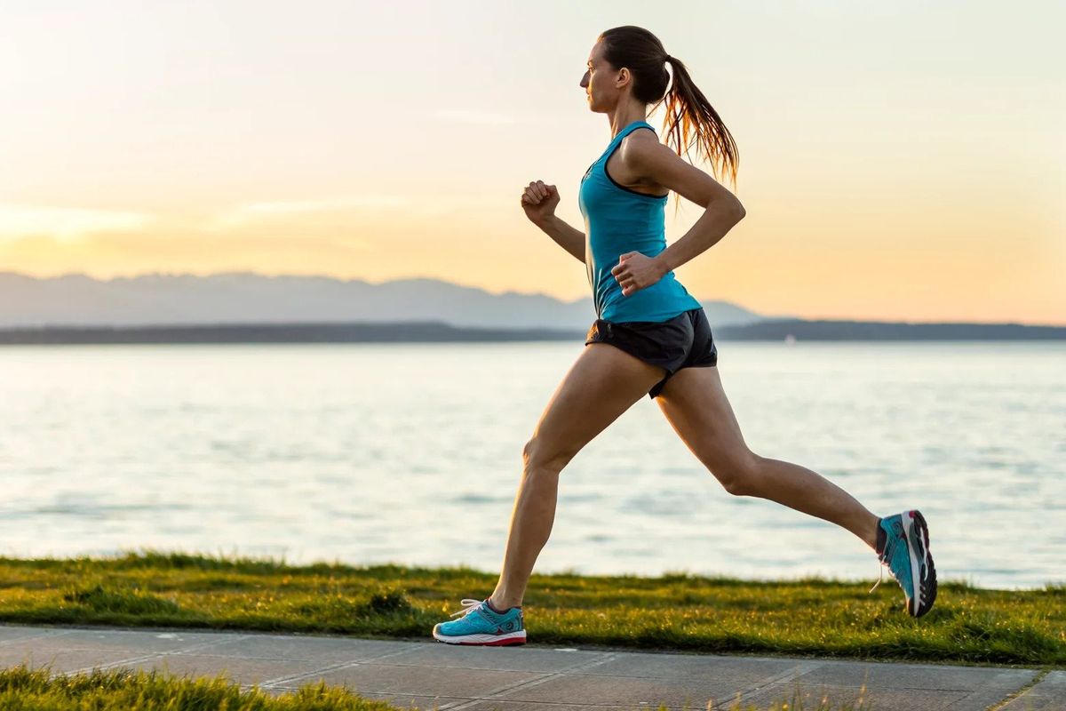 A woman in an aqua top, aqua shoes, and black running shorts runs alongside a river.