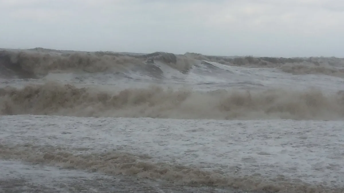 Dark waves roll in toward the camera. The sky is grey.