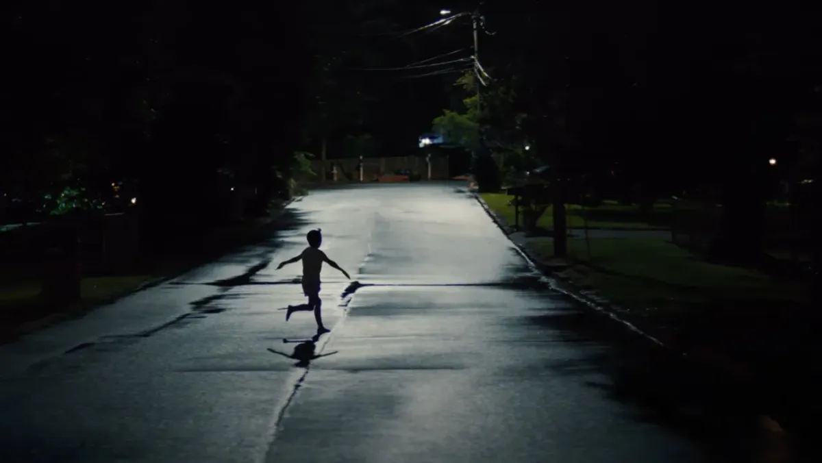 A child runs across a street in silhouette, their arms spread out wide to the side.