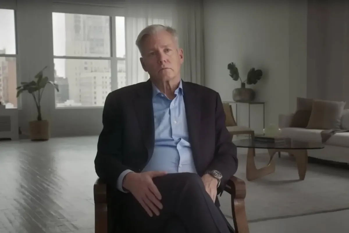 Journalist Chris Hansen, in a suit, sits down for a talking-head interview in a completely beige studio space.