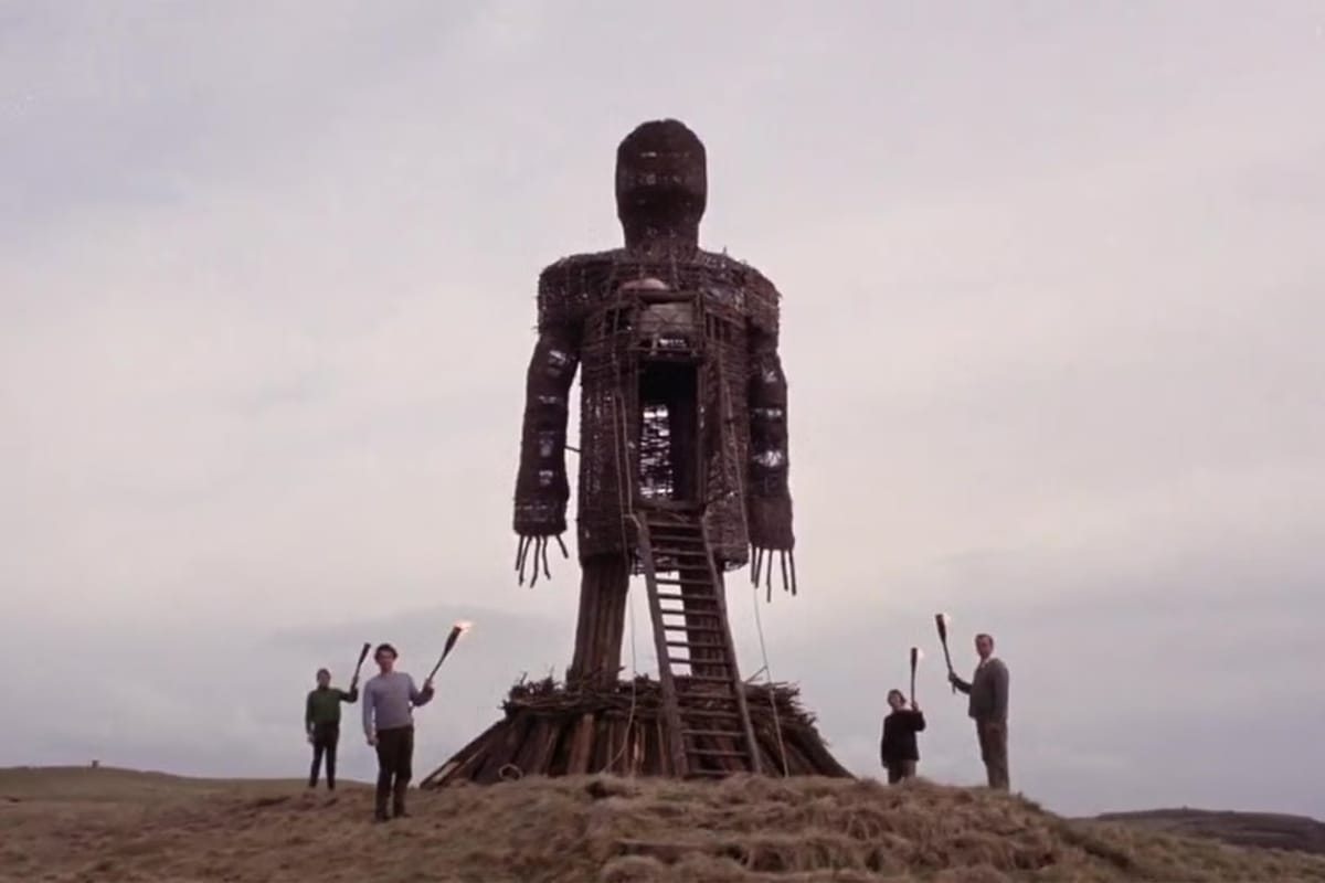 An enormous wicker man stands on a hilltop, surrounded by four smaller figures, all real humans bearing torches.