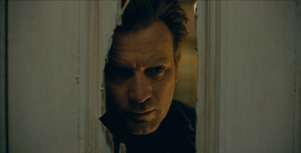Dan (Ewan MacGregor) peers through a hole in a door put there by his axe-wielding father in The Shining.