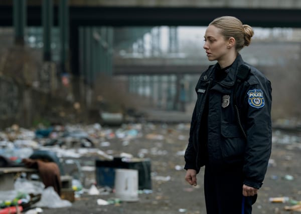 Amanda Seyfried in a Philadelphia police uniform stares with concern at a messy area covered in trash.