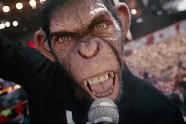A humanoid chimpanzee clutching a microphone sneers at the camera in extreme close-up.