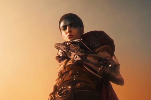 Furiosa, as portrayed by Anya Taylor Joy, looms over the camera. She has a shaved head and a prosthetic arm.