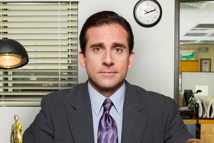 Steve Carell plays Michael Scott in The Office. He's sitting at his desk! 