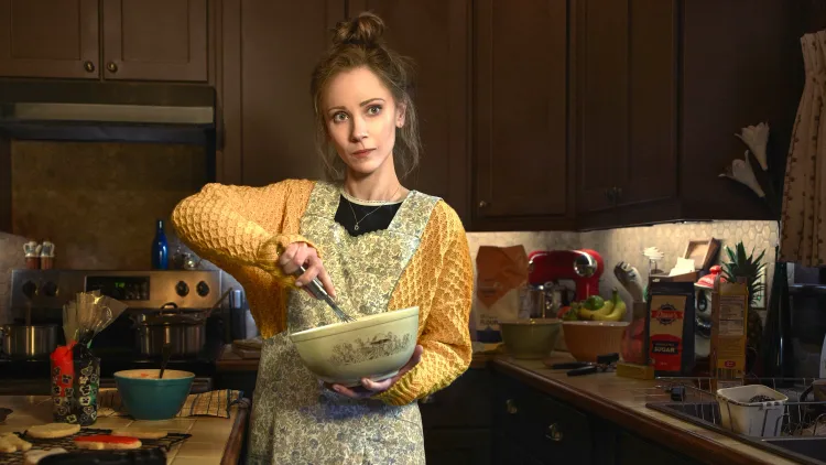 Dot, played by Juno Temple, whisks something together in a ceramic mixing bowl.