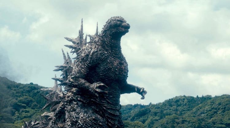 Godzilla rises against a backdrop of forested hills and cloudy sky. He looks mad, but he always looks mad.