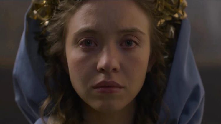 Sydney Sweeney, hair done up in curls, hood around her head, tears up in extreme close-up.