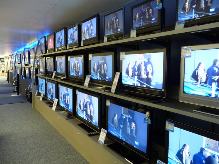 A wall of televisions, all tuned to the same thing, showing a huddle of people.