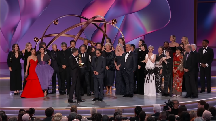 The many actors and people involved in Shogun stand on the purple-hued Emmy stage in their finery.