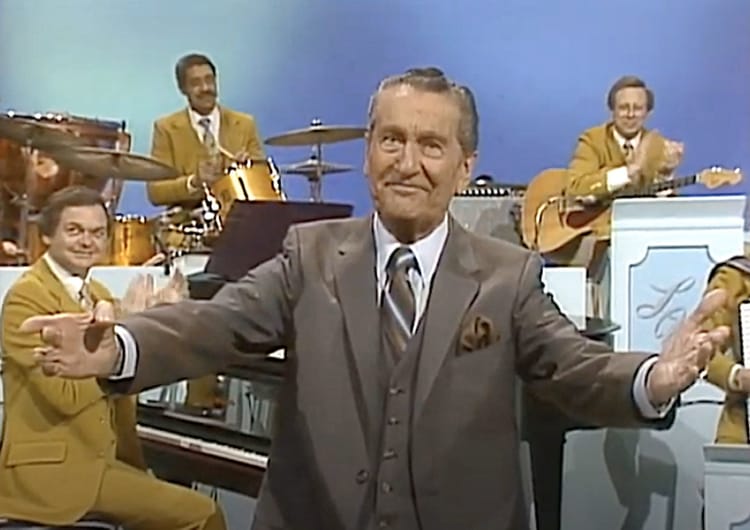 Bandleader Lawrence Welk spreads his arms out wide to celebrate the end of another number.