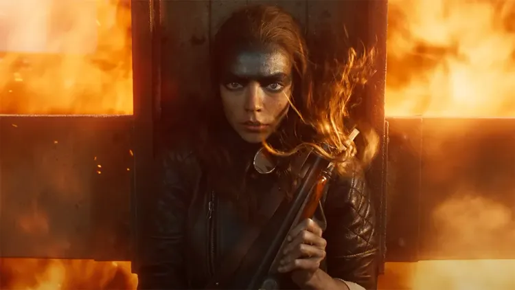 A woman with the top half of her head painted silver hides behind a metal cross. Fire billows around her.