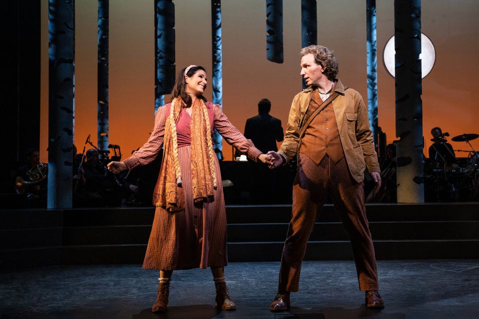 The Baker and his wife hold hands onstage and sing in front of shadowy trees in Into the Woods.