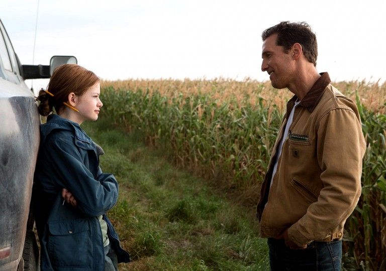 Murph, leans against a pickup near her father, Coop, in Interstellar. They are by a cornfield.