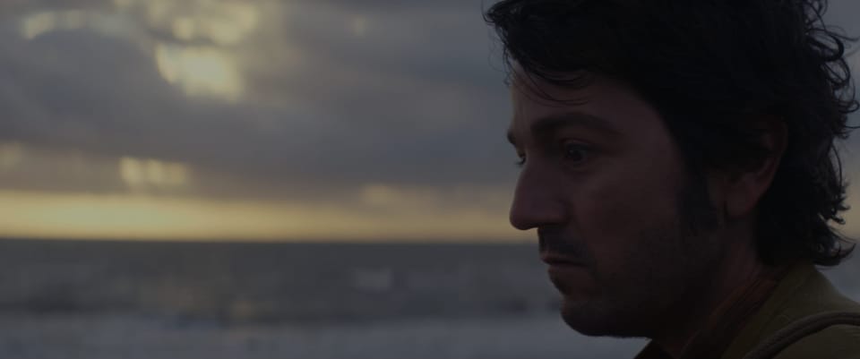 Cassian stares in a melancholy mood as the sun rises behind him. 