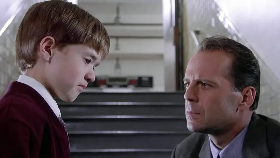 A young boy (Haley Joel Osment) stares down as a man (Bruce Willis) looks at him. They are in a stairwell.