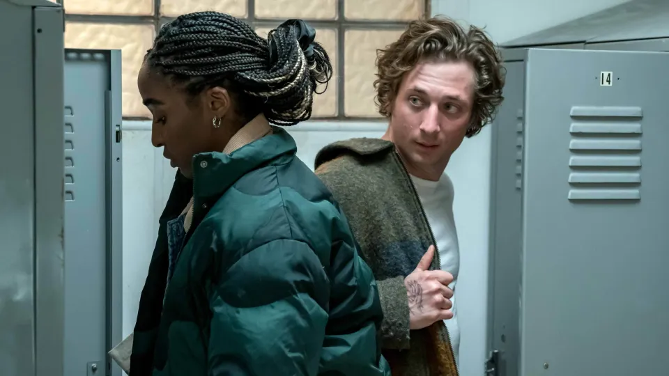 Carmy (Jeremy Allen White) and Syd (Ayo Edibiri) on The Bear get things out of their lockers. He's looking back at her.