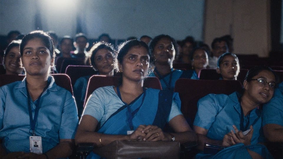 A group of women sit in a movie theater, spellbound by what's on screen. We see the projector's light in the background.