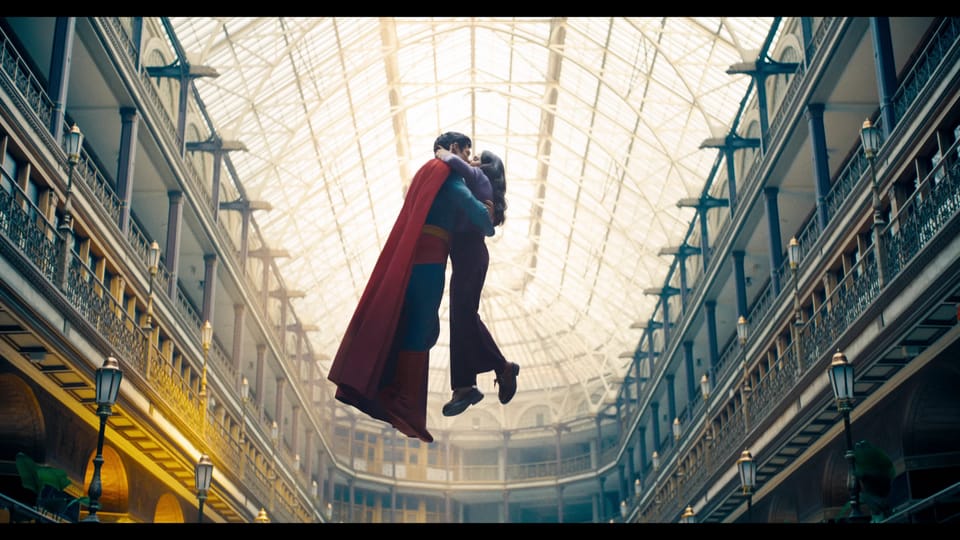 Superman and Lois Lane float off the ground, kissing beneath an enormous glass roof.