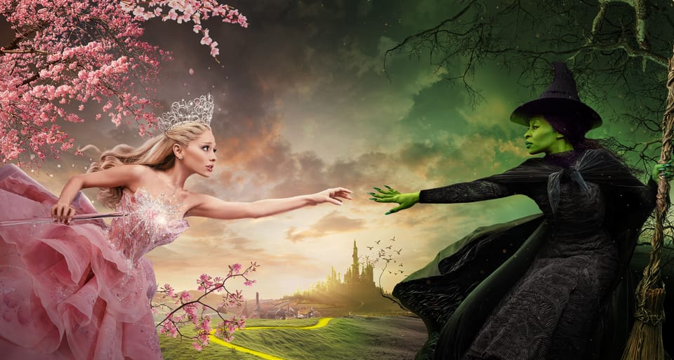 Glinda (all in pink) reaches across open space to Elphaba (in black, skin green) in some Wicked promo art.